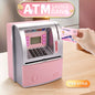 Pink toy ATM savings bank with a hand inserting a card, on a wooden surface.