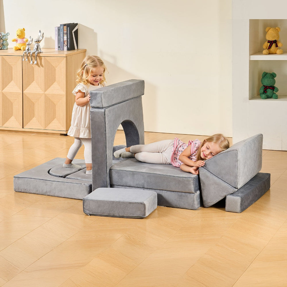 Children playing on a gray modular play set in a room with wooden flooring and shelves.